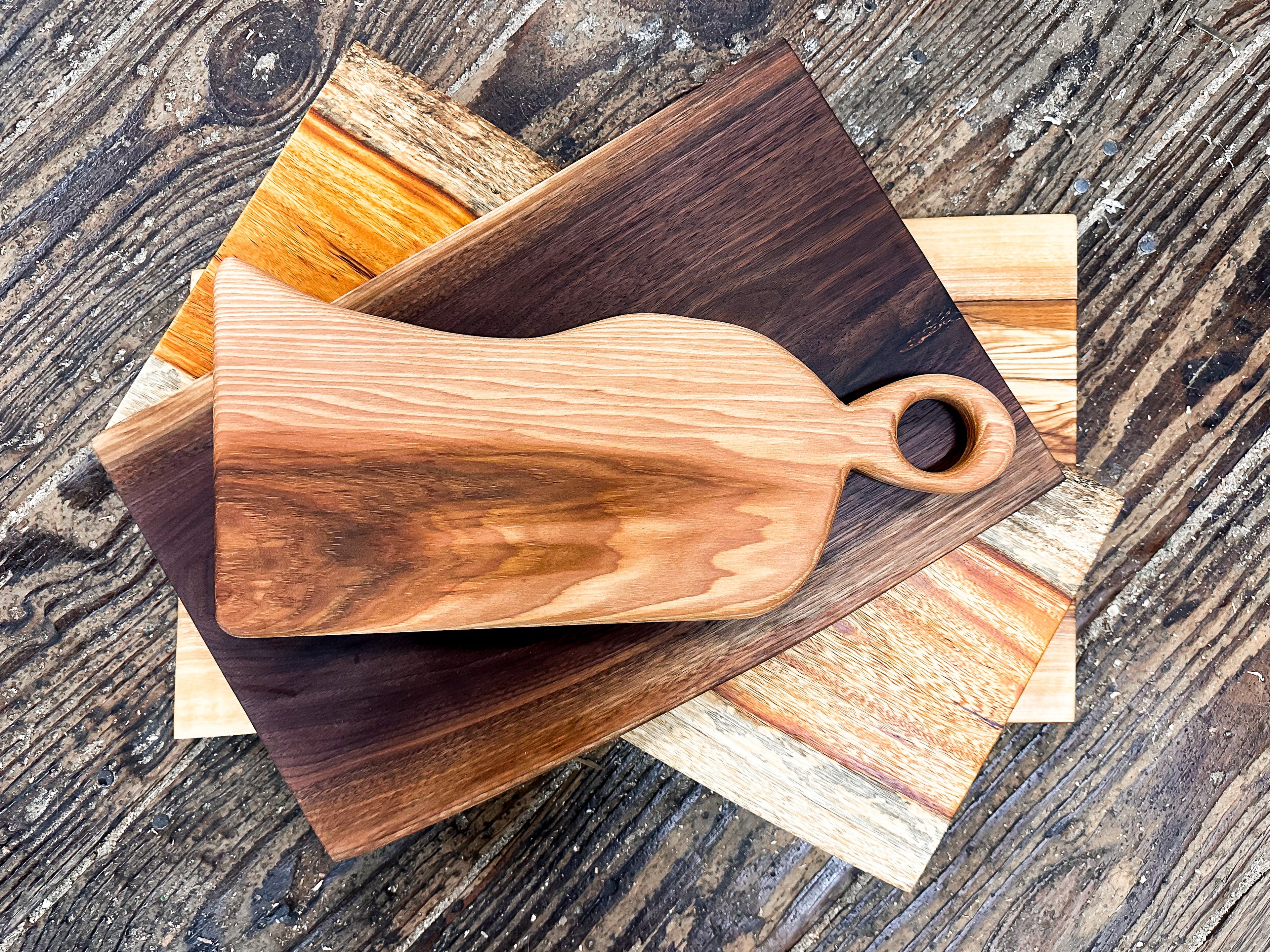 Wooden cutting board with handle on a stack of other wooden boards.